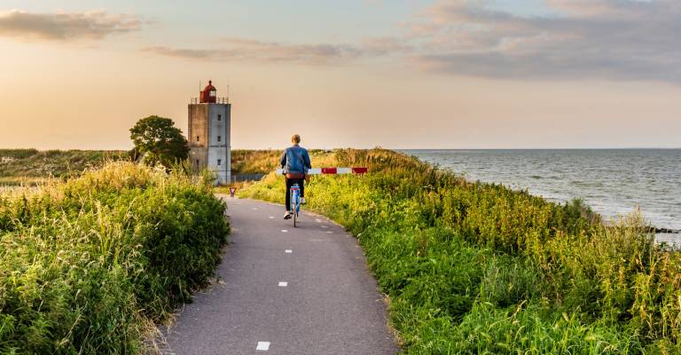 Meisje fietsen naar vuurtoren De Ven bij Edam tijdens zonsondergang in Noord-Holland in Nederland