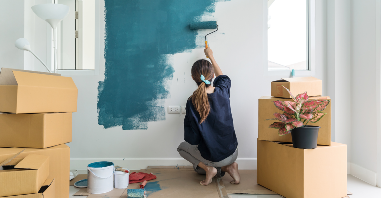 Vrouw schildert een muur blauw van een kamer met dozen op de achtergrond